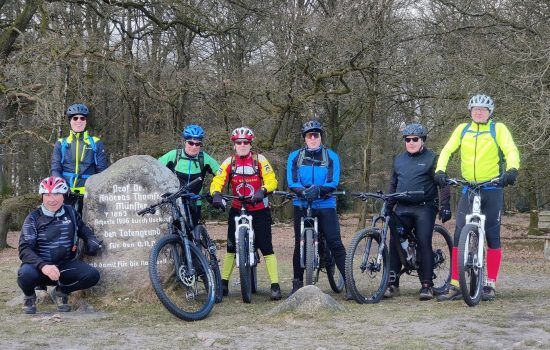 Eine Gruppe von 7 Männern in Mountainbike-Montur, die auf Ihren Fahrrädern sitzen und neben einem Felsen posieren.